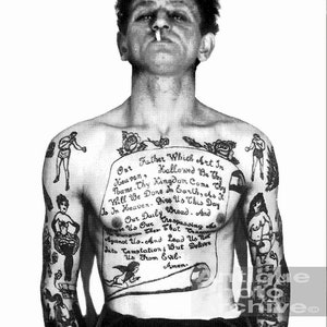 May include: A black and white photo of a man with a full body tattoo. The tattoo includes a traditional style image of a woman, a boxer, a bird, and a scroll with the Lord's Prayer written on it.