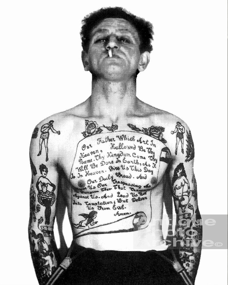 May include: A black and white photo of a man with a full body tattoo. The tattoo includes a traditional style image of a woman, a boxer, a bird, and a scroll with the Lord's Prayer written on it.