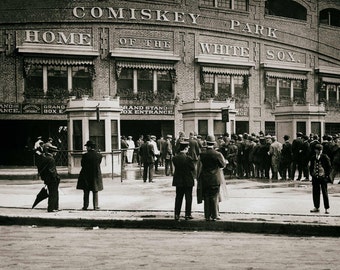 May include: A black and white photo of a crowd of people standing in front of a building. The building has a sign that reads "Comiskey Park, Home of the White Sox".