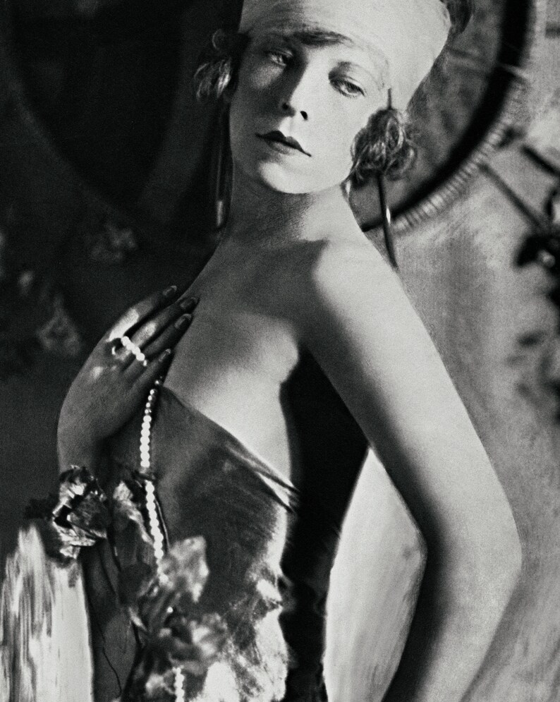 May include: A black and white portrait of a woman wearing a white headband and a beaded necklace. She is looking to the side and has a serious expression on her face.