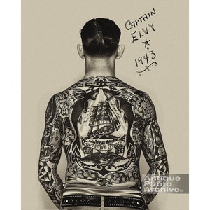 May include: Black and white photo of a man's back with a full body tattoo. The tattoo features a ship, an anchor, and the words "United We Stand". The man's name, "Captain Elvy", and the year "1943" are written on the wall behind him.