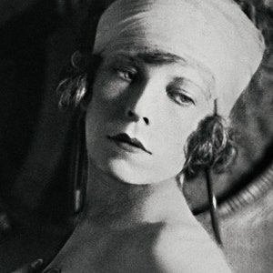 May include: A black and white portrait of a woman with a bandage on her head. The woman is looking to the side and has a serious expression on her face.