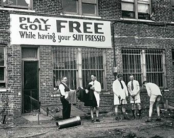 Puede incluir: Fotografía en blanco y negro de un edificio de ladrillo con un letrero que dice "Play Golf Free While having your Suit Pressed". Cinco hombres están de pie frente al edificio, algunos sosteniendo palos de golf.