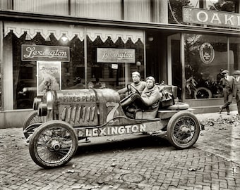 May include: A black and white photo of a vintage Lexington race car with two drivers. The car is decorated with the words "Wins 1st & 2nd at Pikes Peak" and "Lexington".