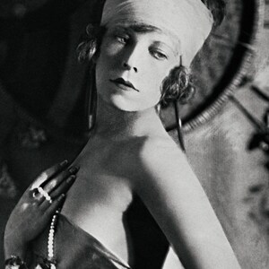 May include: A black and white portrait of a woman wearing a white headband and a pearl necklace. She is looking at the camera with a serious expression.