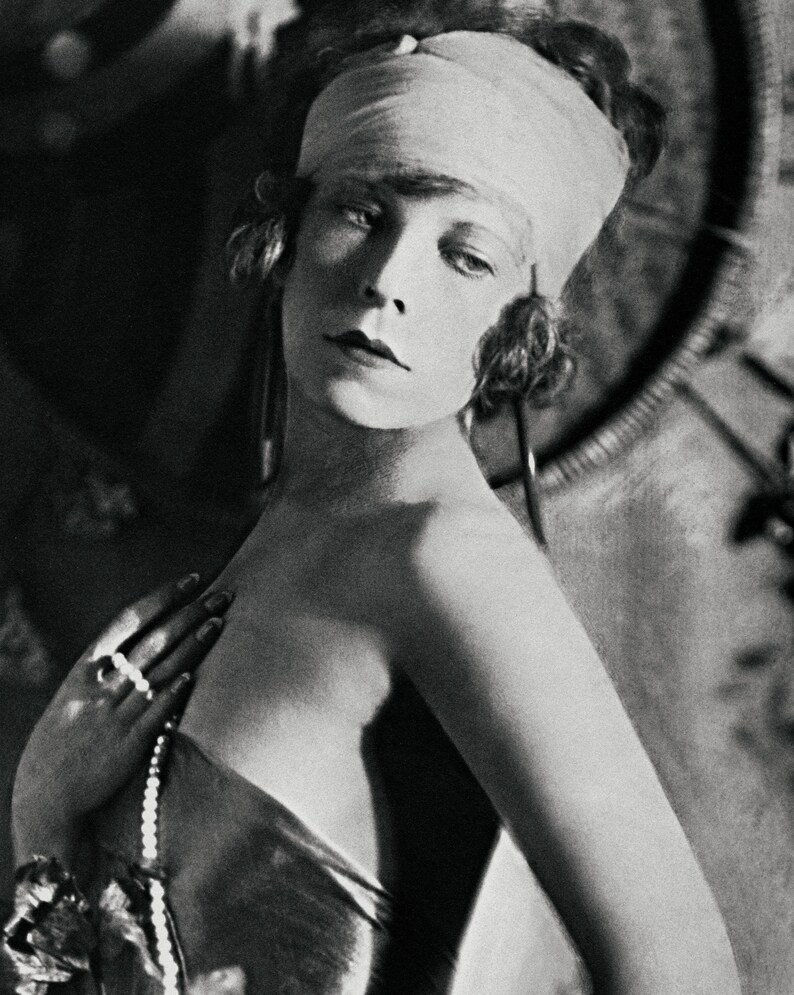 May include: A black and white portrait of a woman wearing a white headband and a pearl necklace. She is looking at the camera with a serious expression.