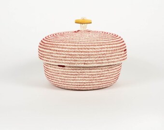 Puede incluir: Una cesta tejida a rayas rojas y blancas con un pomo de madera en la tapa.