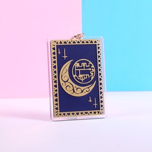 Puede incluir: Una tarjeta azul y dorada con una luna creciente y un símbolo en el centro. La tarjeta está rodeada por un borde dorado.