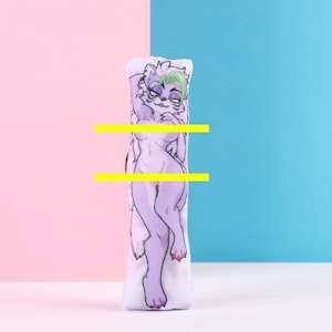 May include: A cylindrical body pillow featuring a stylized illustration of a purple anthropomorphic cat-like creature. The artwork is set against a backdrop of pink and blue, with the pillow standing upright on a white surface.