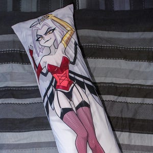 May include: White body pillow featuring a cartoon illustration of a character in a red corset, black lingerie, and fishnet stockings. The character has white hair, yellow eyes, and a gold arm. The pillow is rectangular.