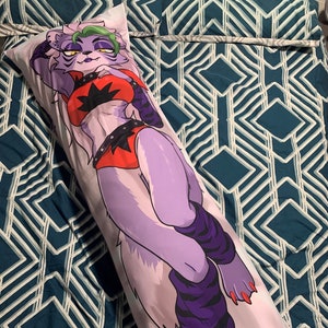 May include: A long body pillow featuring a purple and white cartoon character with green hair, wearing a red and black outfit with a star design. The character is posed with one leg crossed over the other, and the pillow is on a blue and white patterned surface.