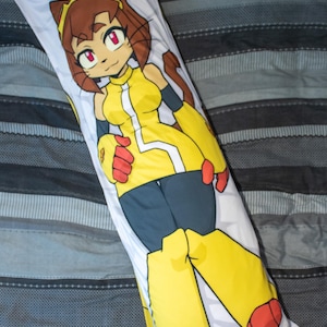 Peut inclure: Un oreiller de corps rectangulaire présentant une illustration imprimée d'un personnage animé aux cheveux bruns, aux yeux rouges et aux oreilles de chat. Le personnage porte un haut jaune sans manches avec une bande blanche, un pantalon sombre, des gants rouges et des bottes jaunes.