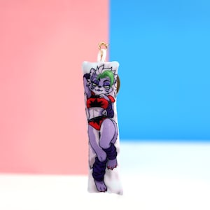 May include: A white plush pillow with a colorful illustration of a purple and green furry character wearing a red and black outfit. The character is posed in a seductive pose. The pillow has a gold loop for hanging.