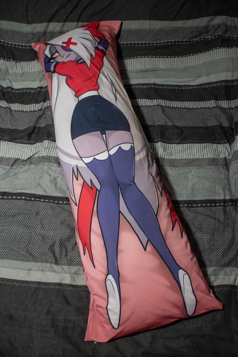 May include: A long, rectangular pillow with a pink background featuring a cartoon character in a red top, black skirt, and purple stockings. The character has white hair and a cross on their forehead.