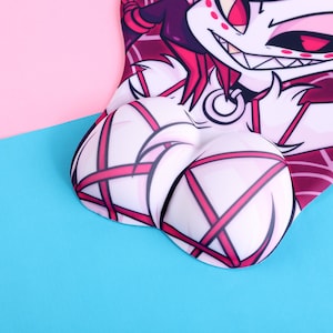 May include: A heart-shaped mousepad featuring a cartoon character with a white face, red eyes, and a wide grin. The mousepad has a built-in wrist rest with a white and pink crisscross pattern. The background is split between pink and blue.