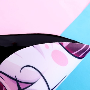 May include: A black, curved object with a white surface featuring a cartoon character design with pink and purple accents. The background is composed of pink and blue sections.