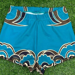 May include: Turquoise athletic shorts with a repeating pattern of brown, black, and white cloud-like shapes. The shorts have an elastic waistband and are made of a smooth, likely synthetic fabric.