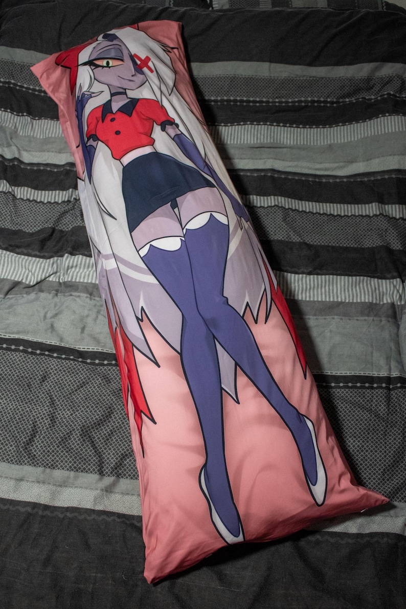 May include: A long, rectangular body pillow featuring a cartoon illustration of a female character. The character has white hair, a red top, and a dark blue skirt. The pillow has a pink background and is on a bed with gray and black striped bedding.