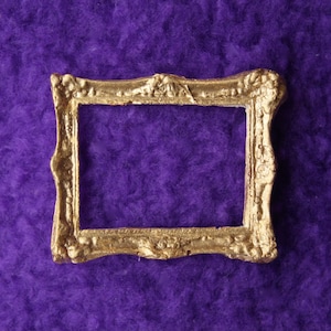 May include: An ornate picture frame in a gold colour with a slightly raised edge. The frame is on a purple background.