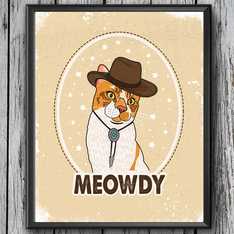 May include: A cartoon illustration of a cat wearing a brown cowboy hat with a turquoise stone on a bolo tie. The cat is surrounded by white stars on a tan background. The text "MEOWDY" is written below the cat.