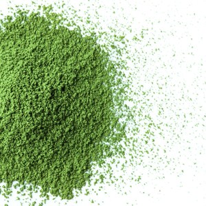 May include: A close-up of a pile of green matcha powder on a white surface. The powder is finely ground and has a light, airy texture.