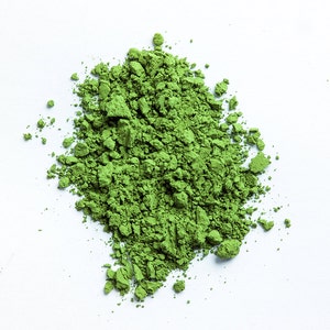 May include: A pile of bright green matcha powder on a white background.