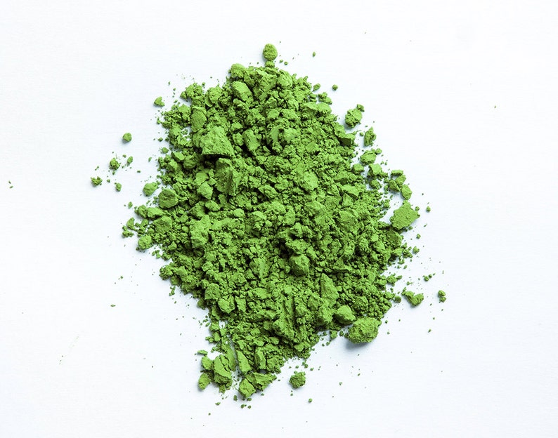 May include: A pile of bright green matcha powder on a white background.