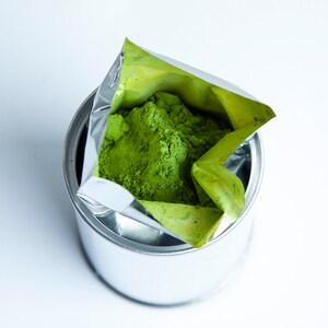 May include: A silver can with green powder inside. The powder is in a foil pouch that is partially pulled out of the can.