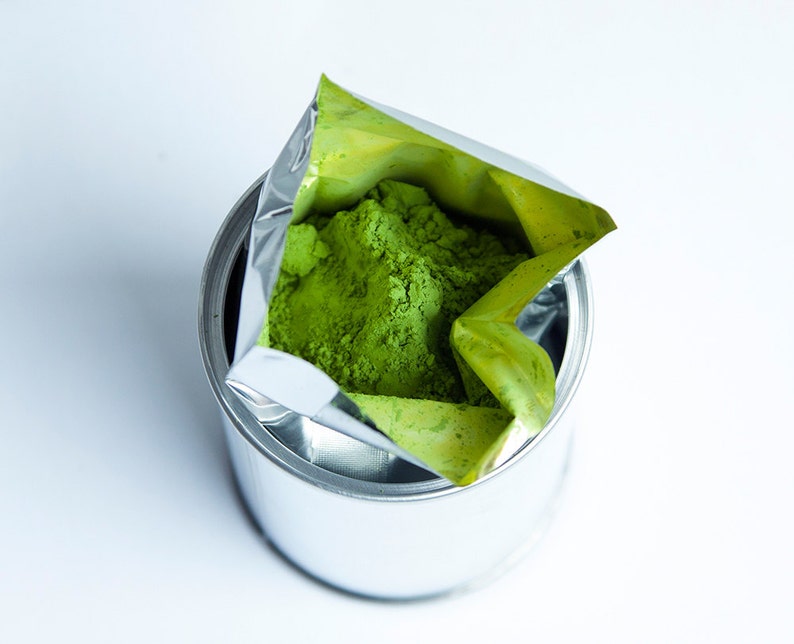 May include: A silver can with green powder inside. The powder is in a foil pouch that is partially pulled out of the can.