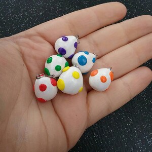 以下が含まれることがあります： 異なる色の水玉模様がついた白い卵型のチャームが6つ。チャームには、吊り下げ用の銀色のジャンプリングが付いています。水玉模様の色は、紫、緑、黄、青、オレンジ、赤です。