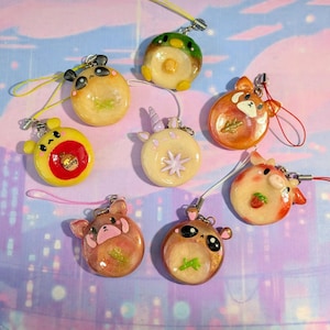 May include: A collection of handmade resin charms in various animal designs, including a panda, red panda, and unicorn. Each charm is round with a glossy finish and features a small loop for attachment. The charms are in shades of yellow, orange, and brown.