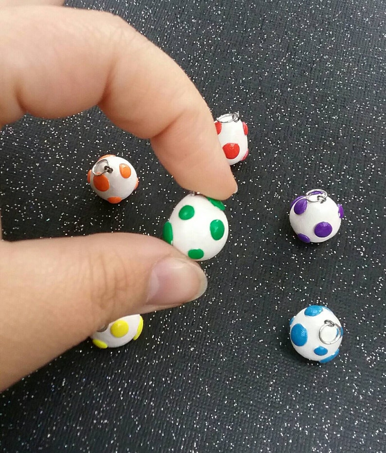 以下が含まれることがあります： 異なる色の水玉模様がついた、小さな白い卵型のチャームが6つ。チャームには、吊り下げ用の銀色のジャンプリングが付いています。