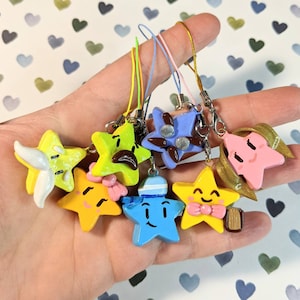 May include: Seven colorful star-shaped charms with different facial expressions. Each charm is attached to a string and has a small loop at the top for attaching to a keychain or bag.