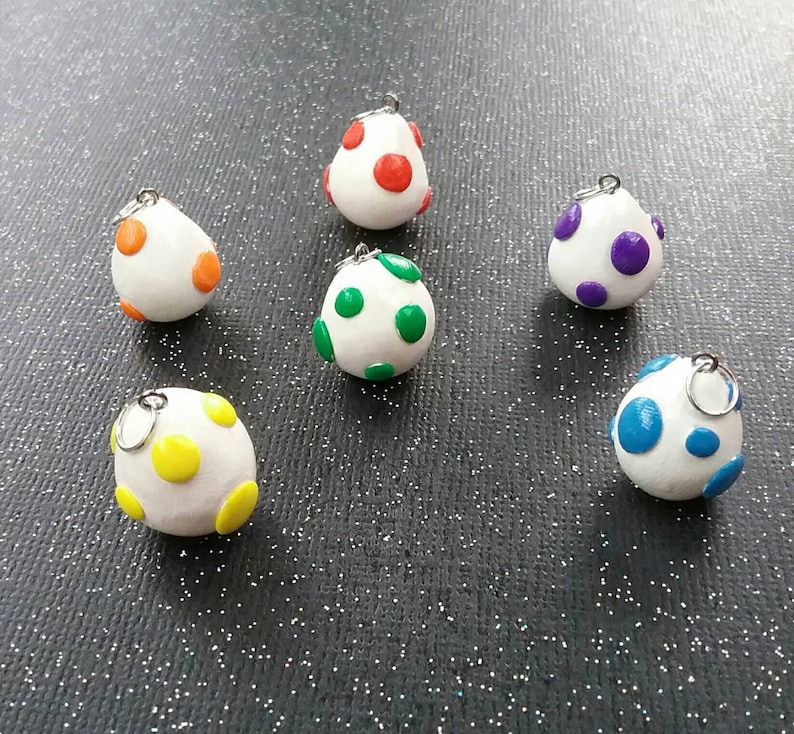 以下が含まれることがあります： 異なる色の水玉模様がついた白い卵型のチャームが6つ。チャームには、吊り下げ用の銀色のジャンプリングが付いています。水玉模様の色は、赤、緑、紫、黄、青です。