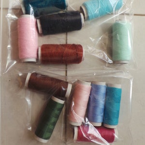 May include: Assortment of colorful spools of thread in various colors, including pink, blue, green, brown, and red. The spools are arranged in a clear plastic bag.