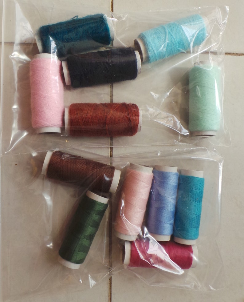 May include: Assortment of colorful spools of thread in various colors, including pink, blue, green, brown, and red. The spools are arranged in a clear plastic bag.