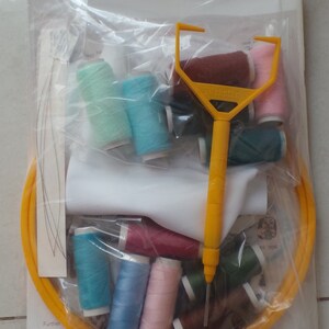 May include: A clear plastic bag containing a variety of embroidery floss spools in different colors, a yellow embroidery hoop, a white fabric square, and a yellow plastic needle threader. The bag also includes a piece of paper with the text "Further A2113 1 A2150 / A2148 S A2147 C A2146 Br".