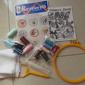 May include: Punchkraft Fun Selection embroidery kit with a white fabric square, a yellow embroidery hoop, and a variety of colored embroidery floss spools. The kit includes a pattern sheet with a cartoon illustration of a cat and a bird.
