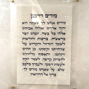 May include: A framed piece of paper with Hebrew text. The text reads "Moddim D'Rabbanan" which translates to "We acknowledge, we thank you." The text continues with a prayer of gratitude.