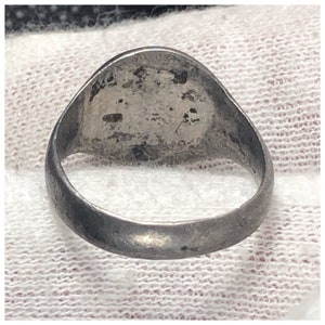 Pu&ograve; includere: Un anello a sigillo d'argento con una parte superiore liscia e arrotondata. L'anello ha un aspetto usurato e antico.