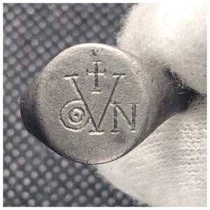 Pu&ograve; includere: Un anello d'argento con un design circolare che presenta una croce e le lettere "VN" incise sulla parte superiore.