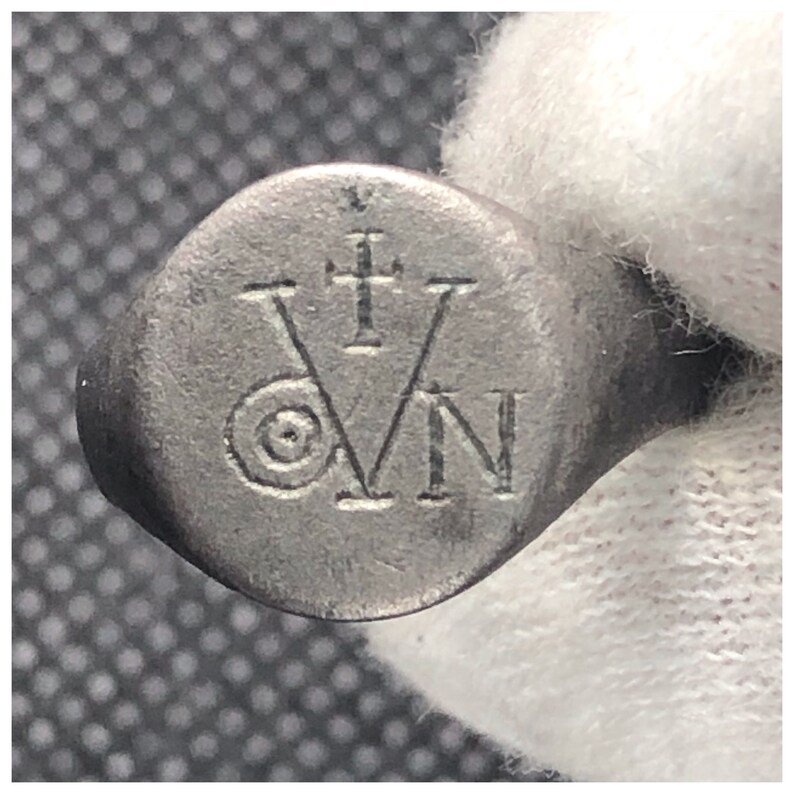 Pu&ograve; includere: Un anello d'argento con un design circolare che presenta una croce e le lettere "VN" incise sulla parte superiore.