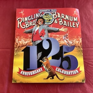 May include: A red, white, and blue poster advertising the 125th anniversary of Ringling Bros. and Barnum & Bailey Circus. The poster features a clown in a red and white costume, a tiger, and the text "The Greatest Show On Earth".