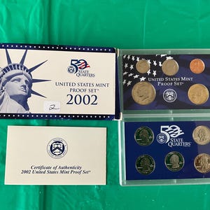 May include: A 2002 United States Mint Proof Set, featuring a box with the Statue of Liberty and the text "50 State Quarters." The set includes various coins in protective cases, and a certificate of authenticity.