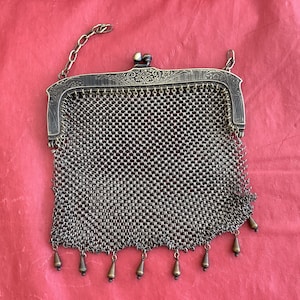 May include: A vintage silver mesh purse with a decorative clasp and a chain strap. The purse has a fringe of small silver beads.