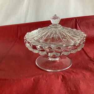 May include: A clear glass candy dish with a lid. The dish has a scalloped edge and a pedestal base. The lid has a knob on top.
