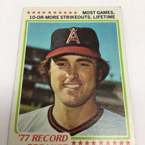 May include: A baseball card featuring Nolan Ryan, a baseball player for the California Angels. The card is from 1977 and features a photo of Ryan in his Angels uniform. The card text reads 'MOST GAMES, 10-OR-MORE STRIKEOUTS, LIFETIME '77 RECORD BREAKER NOLAN RYAN'.