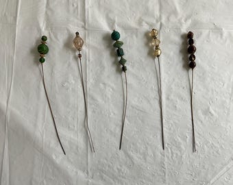 May include: Five decorative wire stems with different colored beads. The stems are all the same length and have a silver finish. The beads are green, brown, clear, and gold.