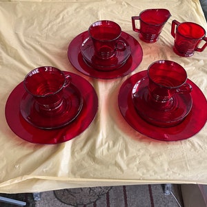 May include: Set of four red glass teacups and saucers with a matching creamer and sugar bowl. The cups and saucers have a simple, elegant design.