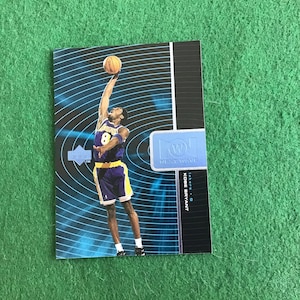 May include: A basketball trading card featuring Kobe Bryant in a purple and gold Lakers uniform, with a blue and white background. The card is part of the "Next Wave" series.